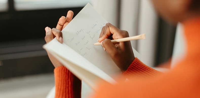 Person in Orange Sweater Writing a Message on a Card Using Pen
